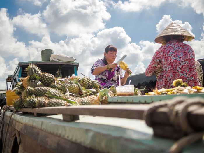 A woman cutting pineapples on the river.